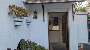 A white building with a tiled roof, a wooden gate, and potted plants.