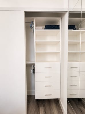 A white closet with open shelves and drawers, a wooden floor, and a mirror. - Downtown Calgary Haven - Steps to Stampede (Calgary)