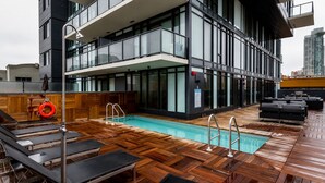 A rooftop pool area with wooden decking, lounge chairs, and a lifebuoy. - Downtown Calgary Haven - Steps to Stampede (Calgary)