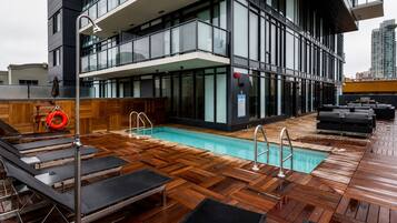 A rooftop pool area with wooden decking, lounge chairs, and a lifebuoy.