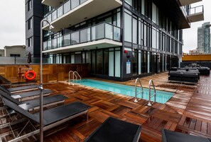 A rooftop pool area with wooden decking, lounge chairs, and a lifebuoy. - Downtown Calgary Haven - Steps to Stampede (Calgary)
