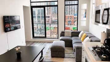 A modern apartment with a large living area, a dining table, a kitchen with a stove, and large windows offering views of the city.