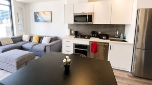 A modern kitchen with white cabinets, a stainless steel refrigerator, and a dining area with a black table. - Downtown Calgary Haven - Steps to Stampede (Calgary)