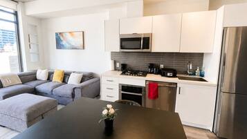 A modern kitchen with white cabinets, a stainless steel refrigerator, and a dining area with a black table.
