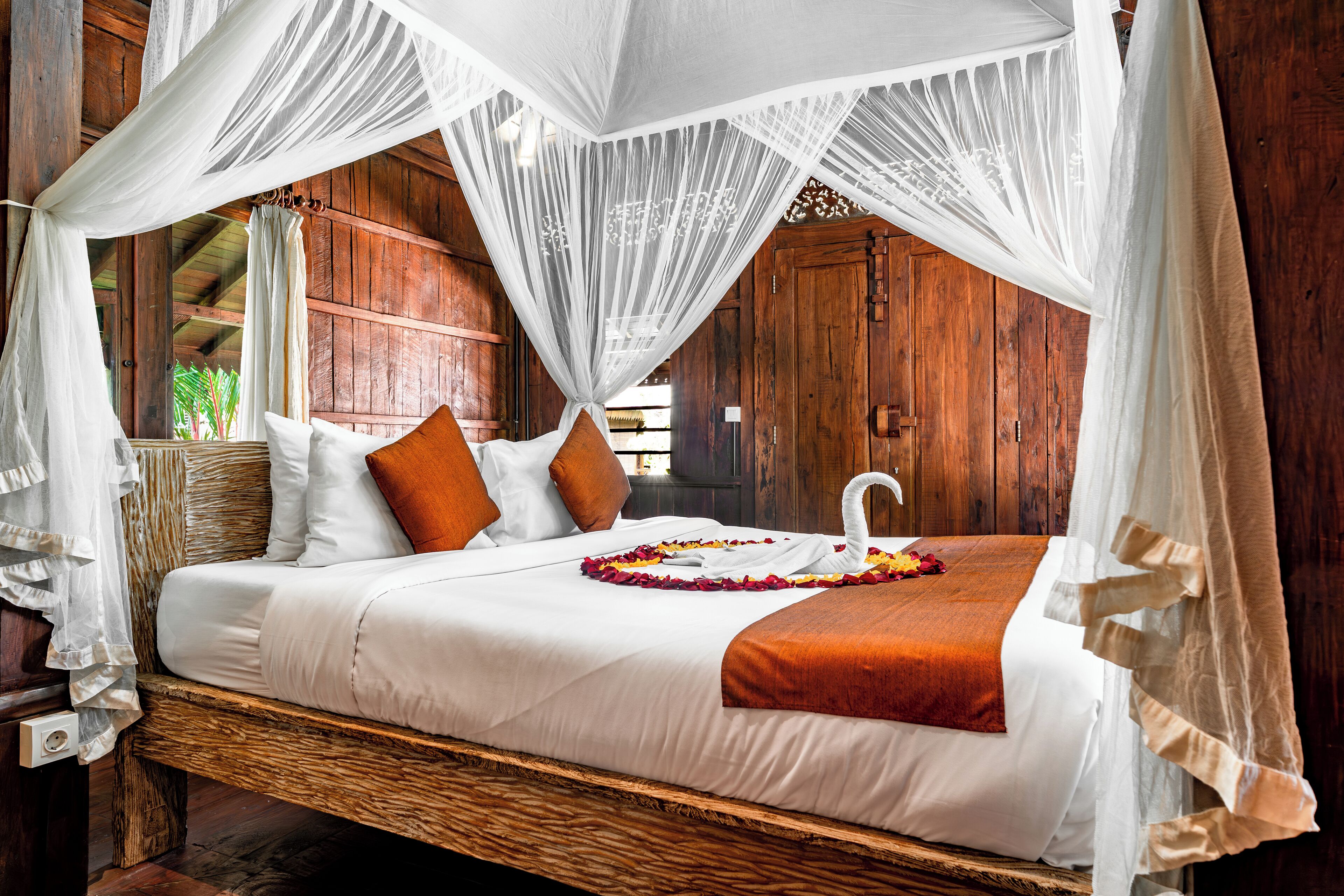 A bed with white linens, orange pillows, and a swan-shaped towel centerpiece.