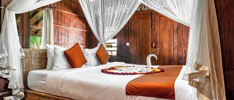 A bed with white linens, orange pillows, and a swan-shaped towel centerpiece.
