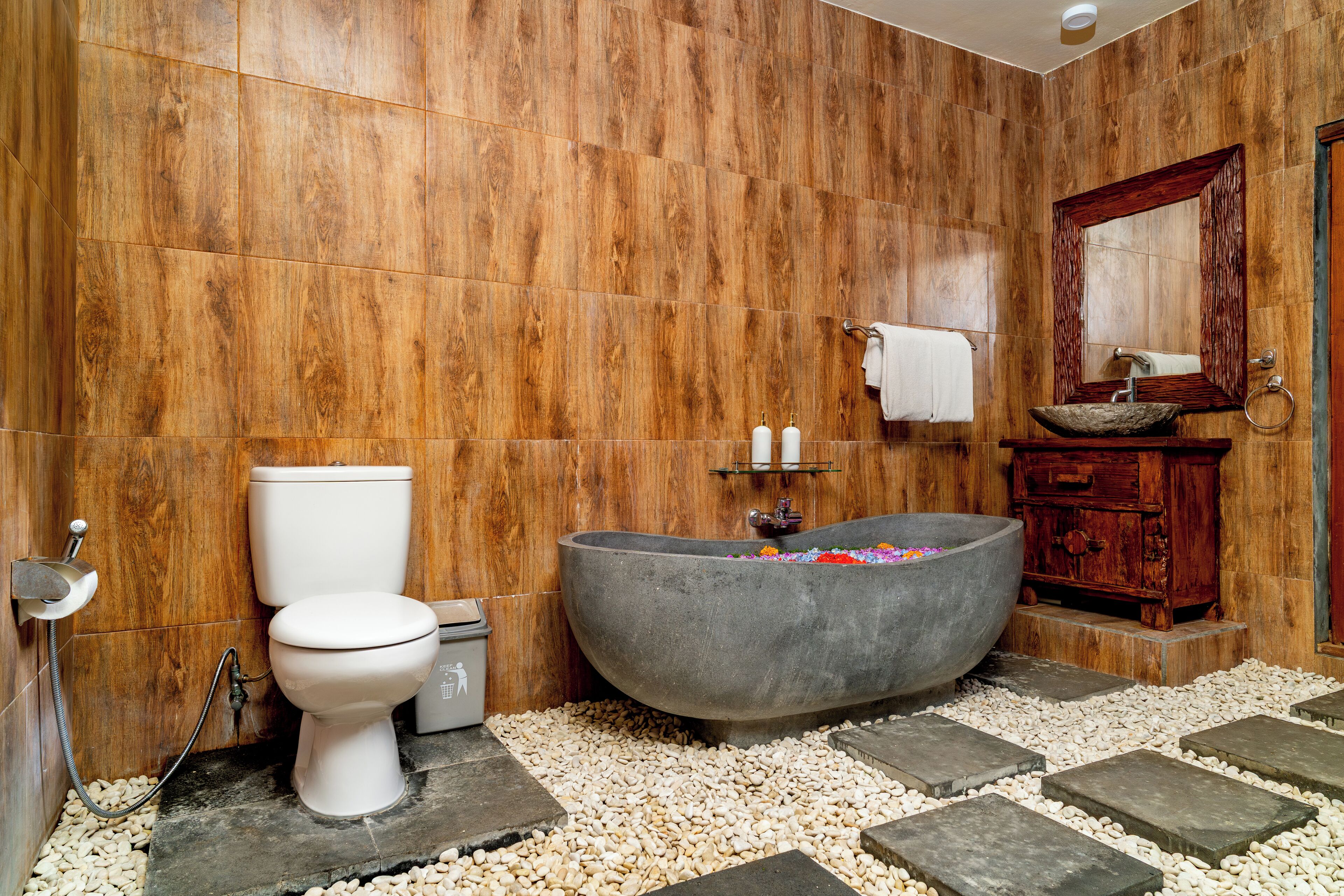 A bathroom with a wooden wall, a white toilet, a freestanding bathtub, and a wooden vanity with a mirror.