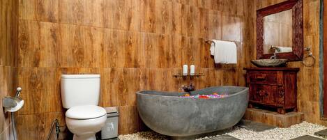 A bathroom with a wooden wall, a white toilet, a freestanding bathtub, and a wooden vanity with a mirror.