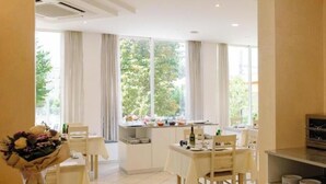 A modern dining area with a table set for two, a vase with flowers, and a kitchen counter with dishes. - Cà d'Oro (Rimini)