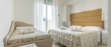 Habitación de hotel con dos camas, un ventanal con cortinas, una mesita de noche con lámpara y un armario.