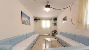 A room with a long light blue sofa, a small white table, and a projector mounted on the ceiling. - Cà d'Oro (Rimini)
