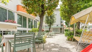 An outdoor patio area with tables and chairs, a slide, and a building with balconies and windows. - Cà d'Oro (Rimini)