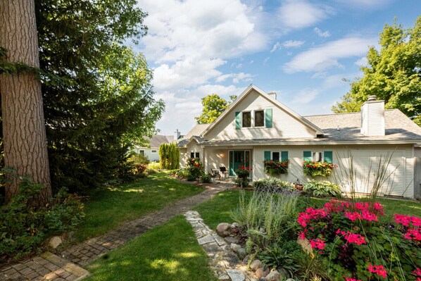 A single-story house with a front porch, a well-maintained lawn, and a variety of flowering plants.