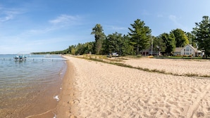 A sandy beach with a row of houses and a pier extending into calm water.