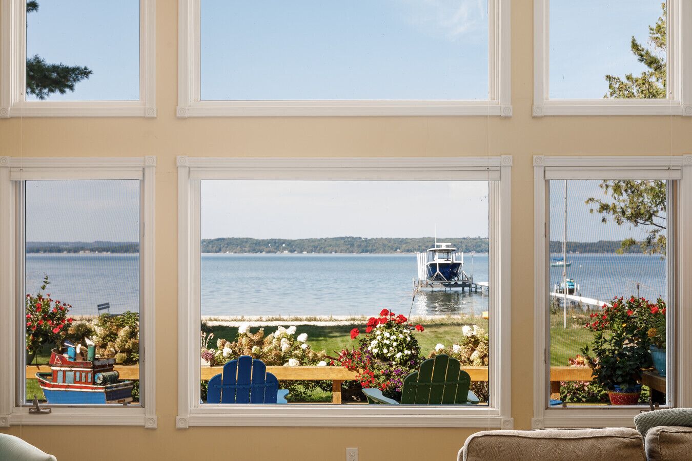 A room with three large windows overlooking a lake, a dock, and a boat.