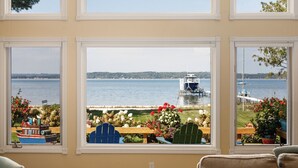 A room with three large windows overlooking a lake, a dock, and a boat.