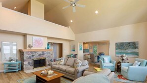A spacious living room with a stone fireplace, a high ceiling, and a view of the ocean.