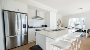 A modern kitchen with a stainless steel refrigerator, white cabinets, a gas stove, and a large island with bar stools.