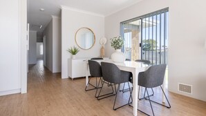 A modern dining area with a white table, four grey chairs, a round mirror, and a potted plant.