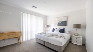 A bedroom with a bed, bedside tables, a desk, and a large window with blinds.