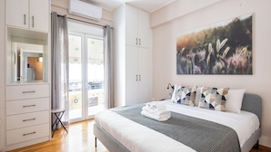 A bedroom with a bed, a wardrobe, a small table, and a large window. - Selany's Chic Apt in the Heart of Athens (Athens)