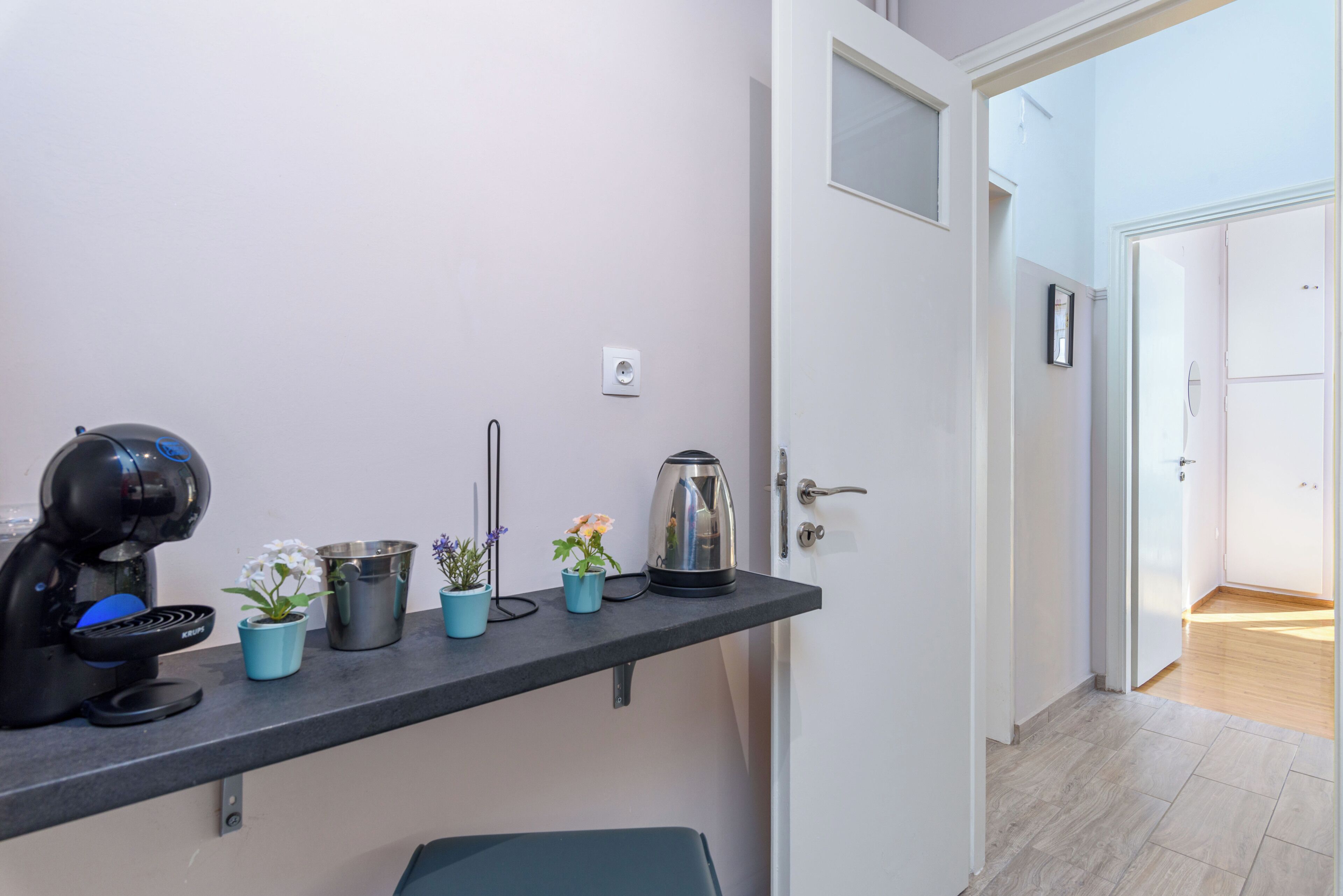 A kitchenette with a coffee maker, kettle, and potted plants on a countertop.