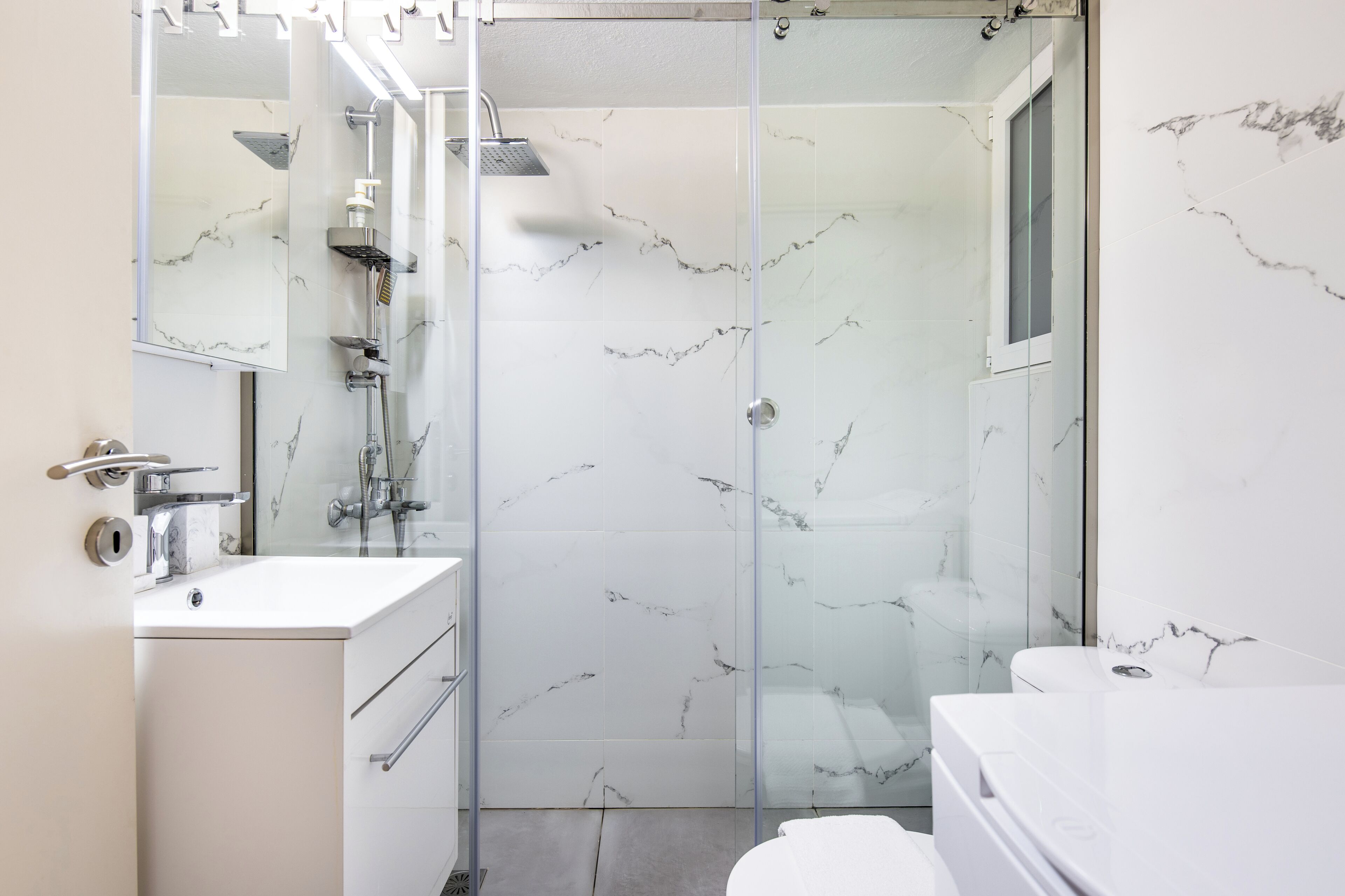 A modern bathroom with a glass shower enclosure, a white sink, and a large mirror.