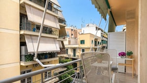 A balcony with a wicker chair, a small table with a vase of flowers, and a view of neighboring buildings. - Selany's Chic Apt in the Heart of Athens (Athens)