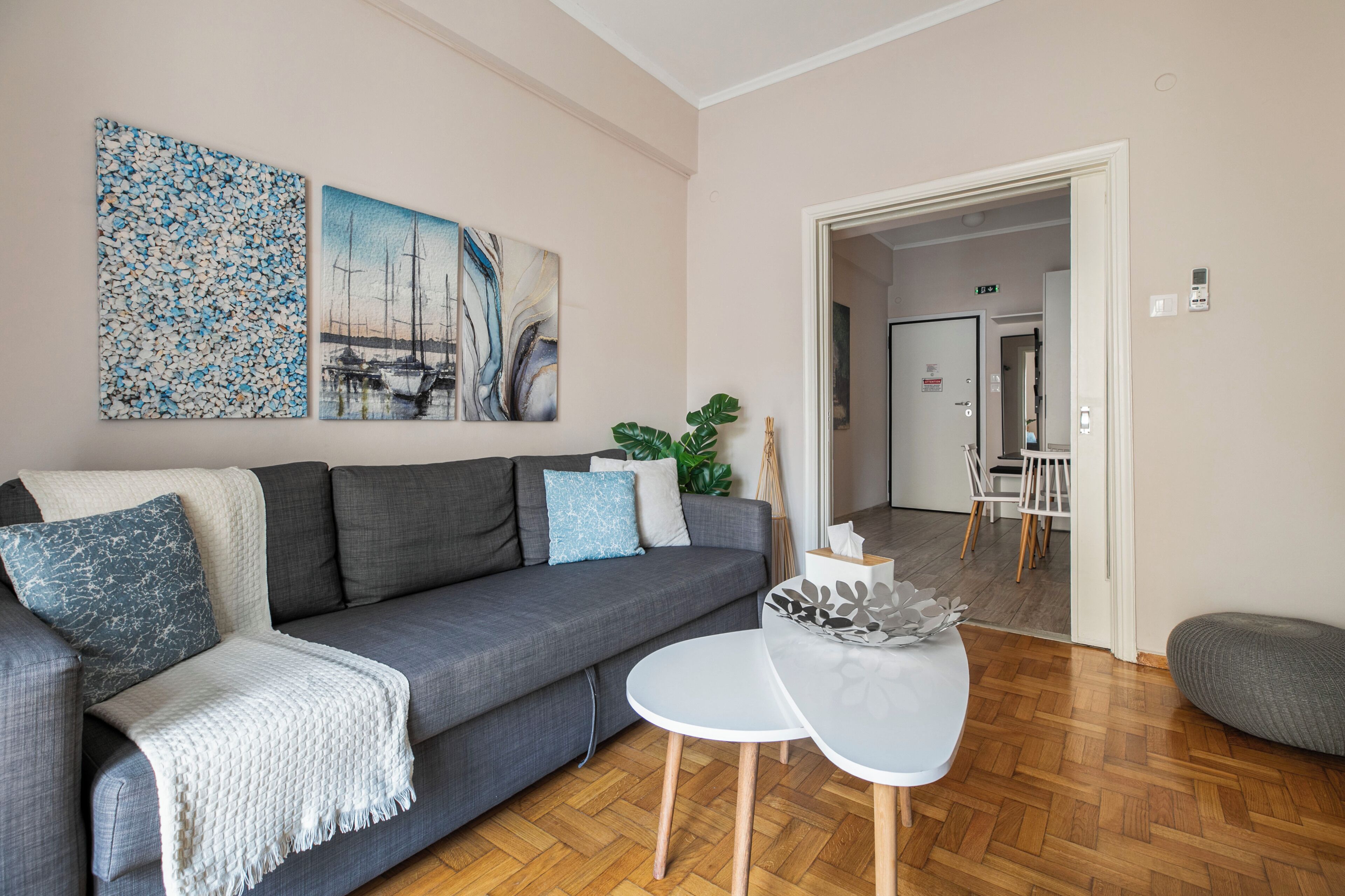 Un salon moderne avec un canapé gris, une table basse blanche et des œuvres d’art accrochées au mur.