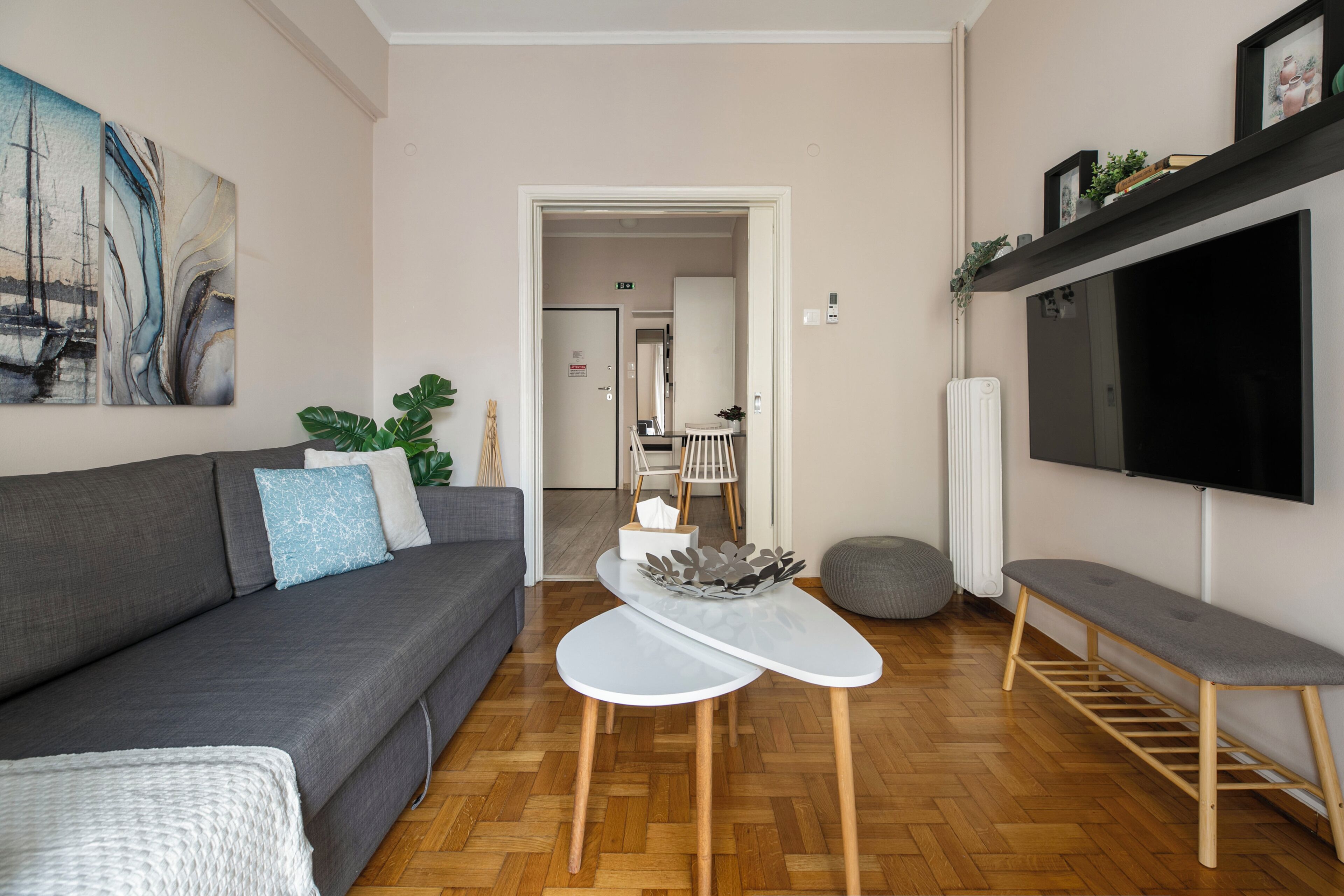 A modern living room with a grey sofa, a white coffee table, a bench, and a TV mounted on the wall.
