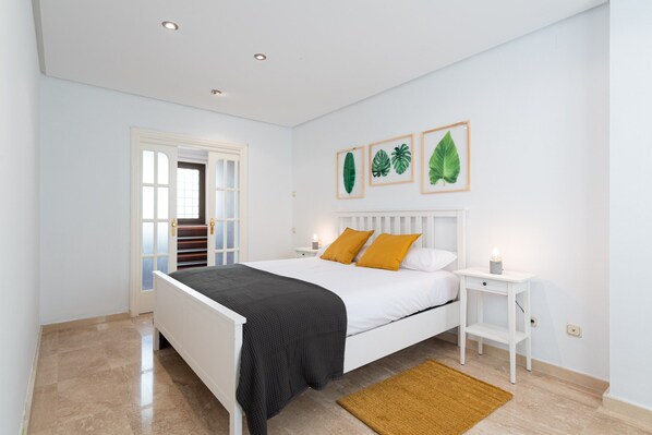 A bedroom with a white bed, two nightstands, a door, and three framed leaves on the wall. - Beachfront House in Las Palmas With Terrace (Las Palmas de Gran Canaria)