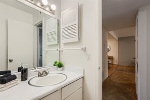 A modern bathroom with a large mirror, white sink, and a small potted plant.