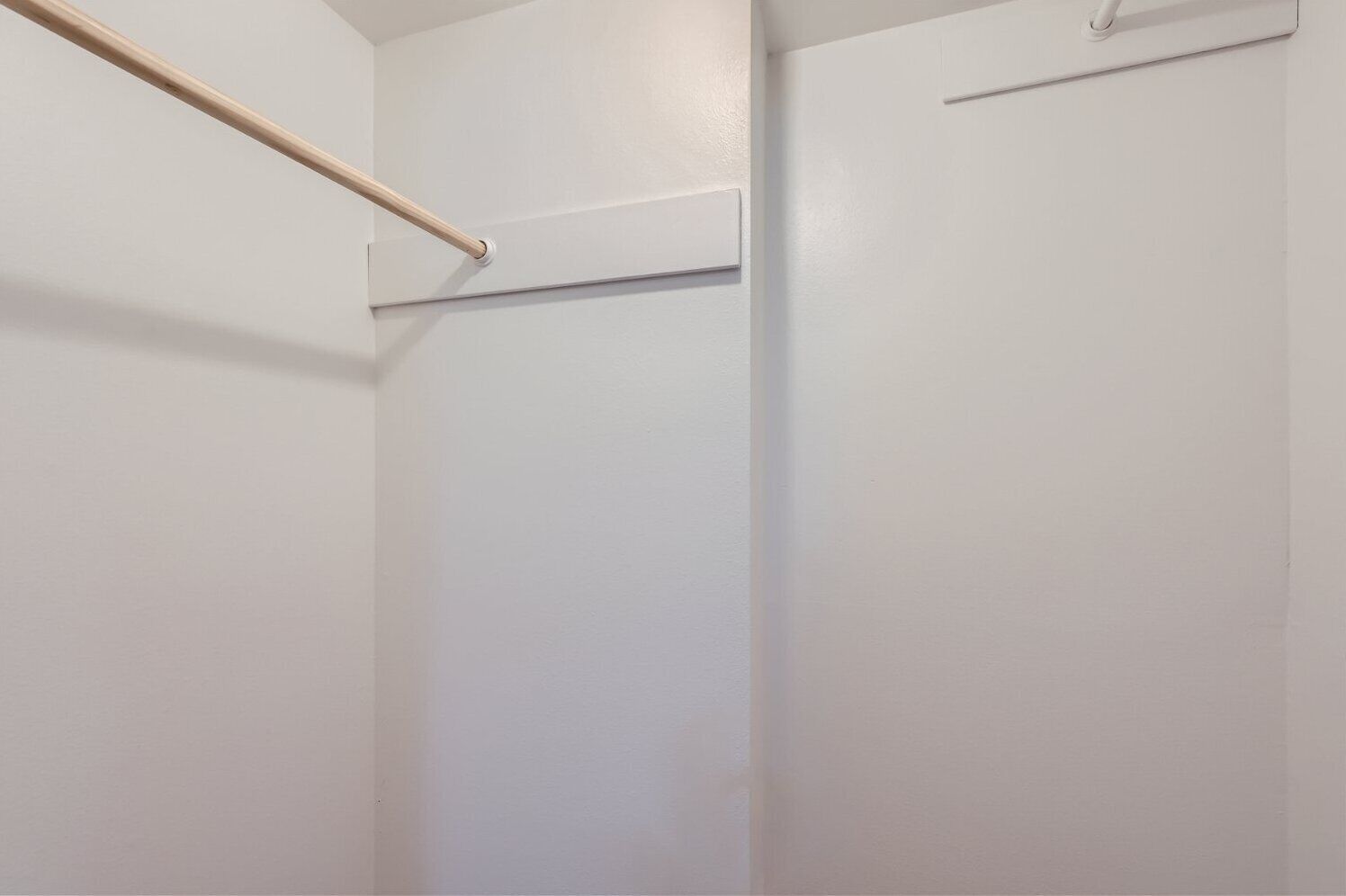 A white interior space with a wooden rod and a horizontal bar, likely part of a closet or storage area.