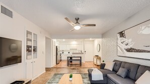 Un salon moderne avec un canapé gris, une table basse en bois et un téléviseur placé à gauche.