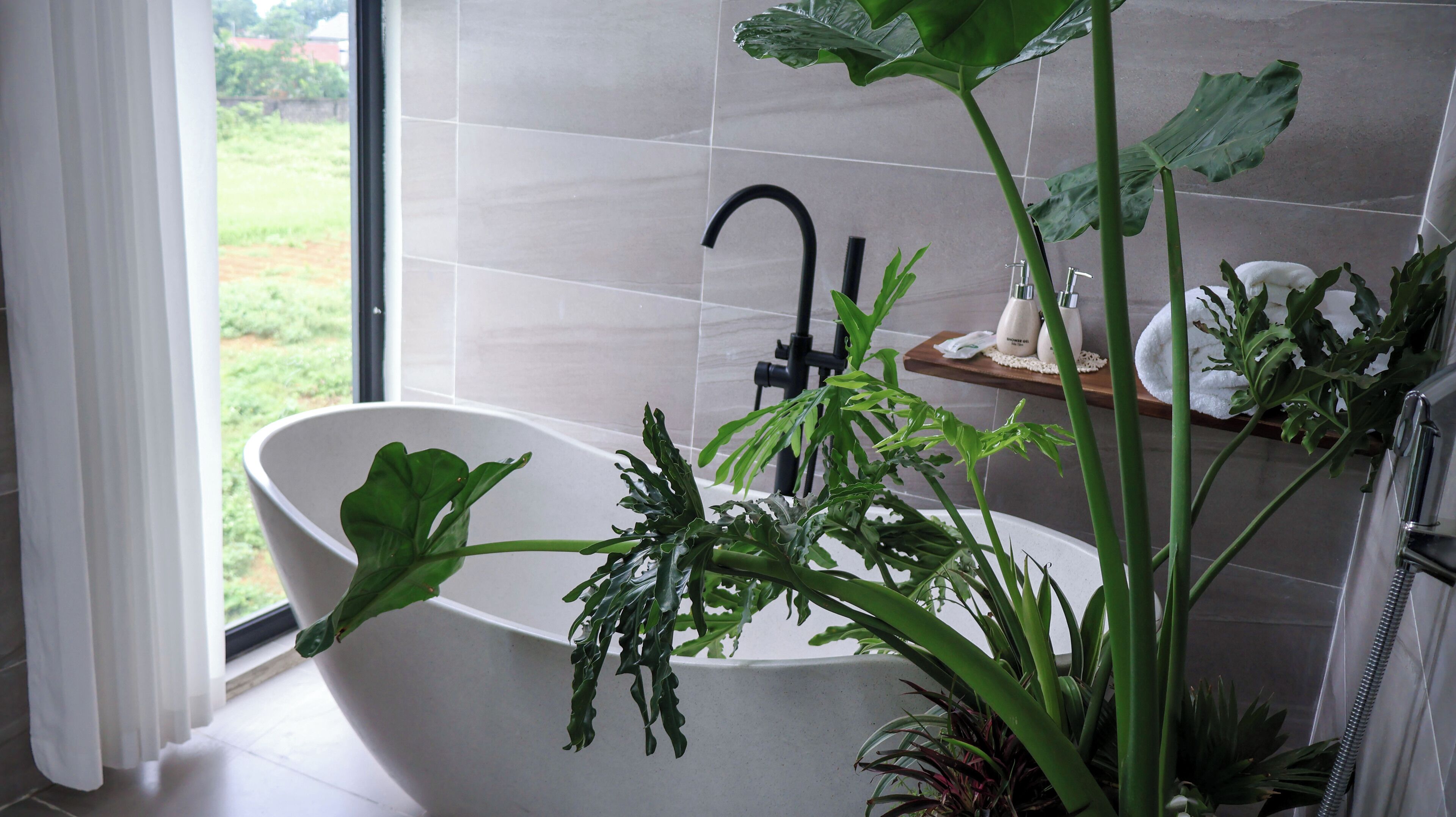 A modern bathroom with a freestanding bathtub, a large window, and a view of the outdoors.