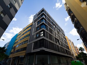 Ein modernes, mehrstöckiges Gebäude mit Hauseingang an einer Ecke, großen Fenstern und einer flachen Dachfläche.