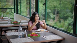 Ένας χώρος τραπεζαρίας με τραπέζια στρωμένα για το γεύμα, ένα μπουκάλι νερό και ένα πιάτο με φαγητό.