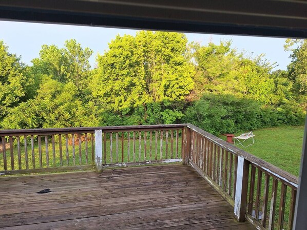 A wooden deck with a railing, overlooking a grassy yard with trees and a chair.