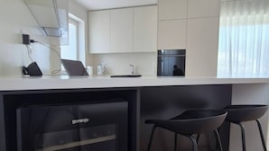 Una cocina compacta con refrigerador integrado, microondas y pileta. Hay dos taburetes negros y una ventana con cortinas.