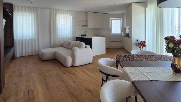 Un amplio salón con piso de madera, un sofá, una mesa de comedor con sillas y una cocina al fondo.
