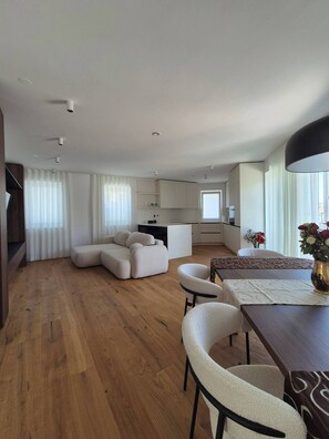 A spacious living area with a wooden floor, a sofa, a dining table with chairs, and a kitchen in the background. - 3-bedroom condo in enchanting Ljubljana with AC, WiFi. Relax and enjoy (Ljubljana)