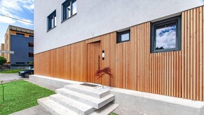 Un edificio moderno con fachada de madera, escalones de hormigón que conducen a la entrada y un cielo despejado.