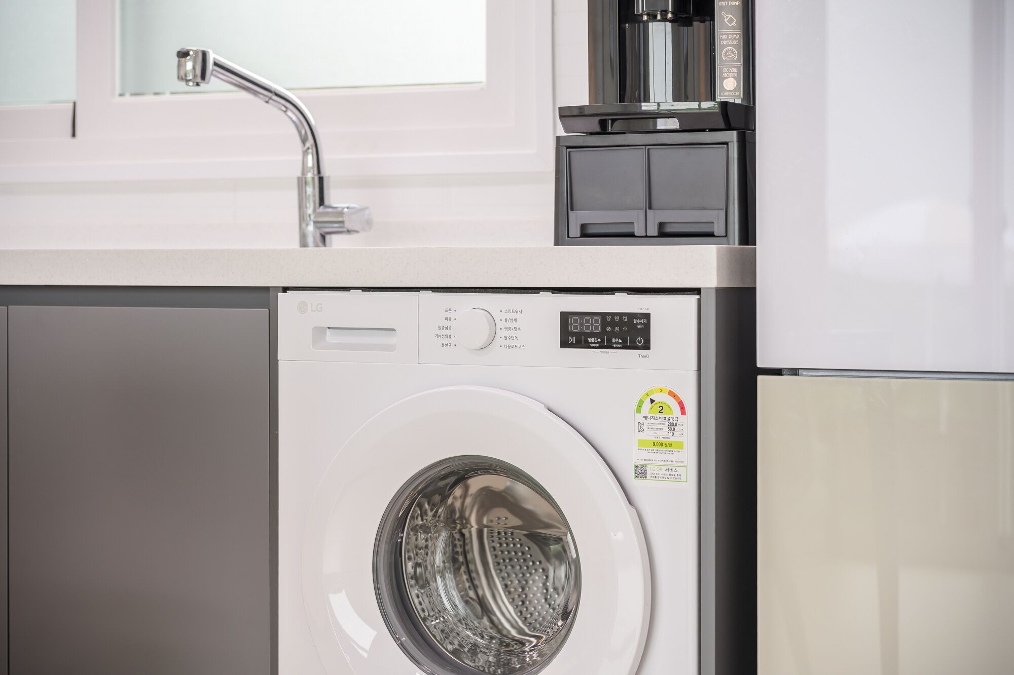A compact washer and dryer unit with a control panel, a water dispenser, and a small window above the sink.