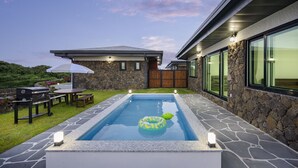 A swimming pool with a stone deck, a barbecue grill, and a covered patio area. - Gimnyeong stonewall Private Pool Villa (Jeju City)