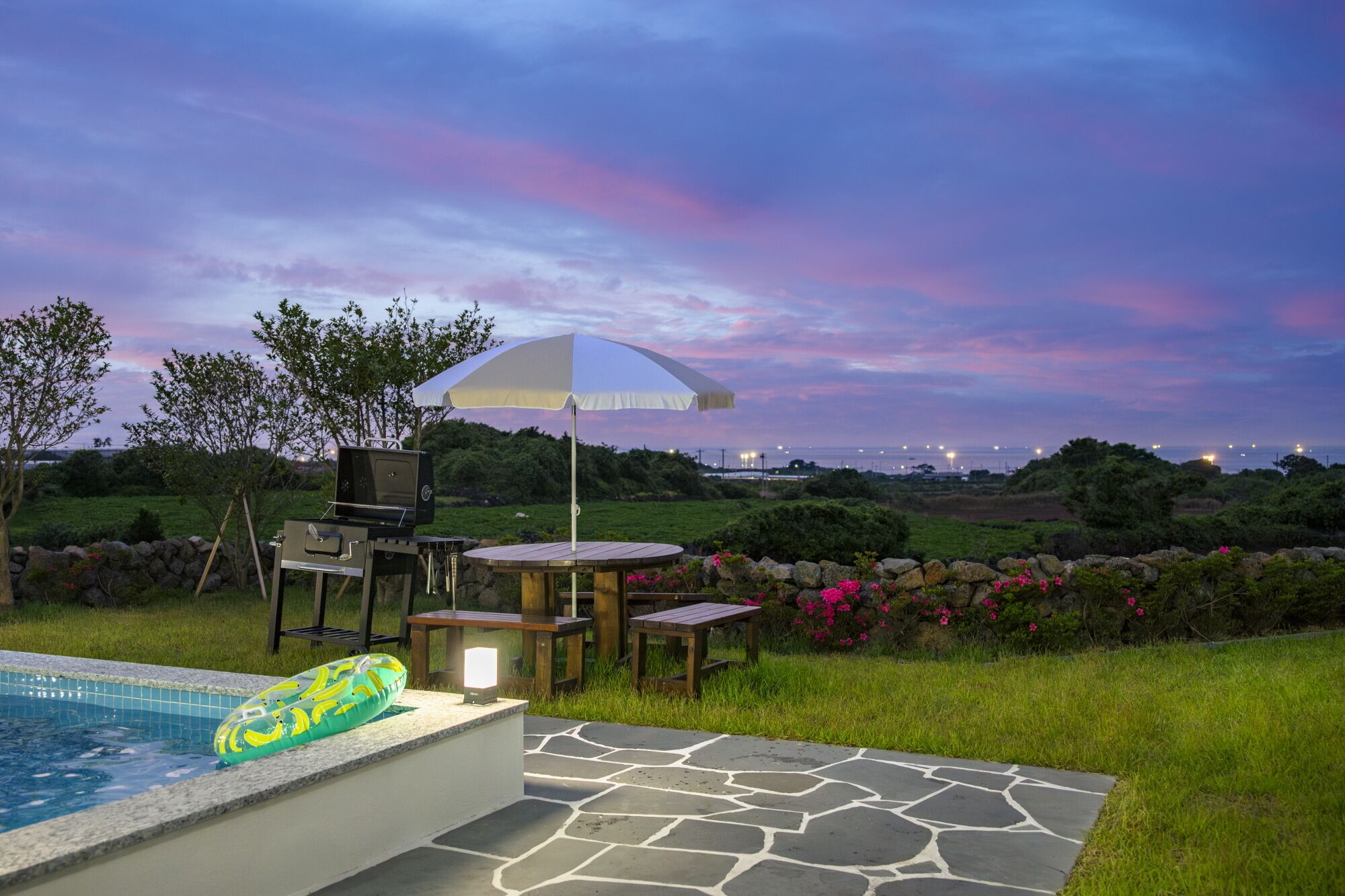 A poolside area with a grill, umbrella, and seating.
