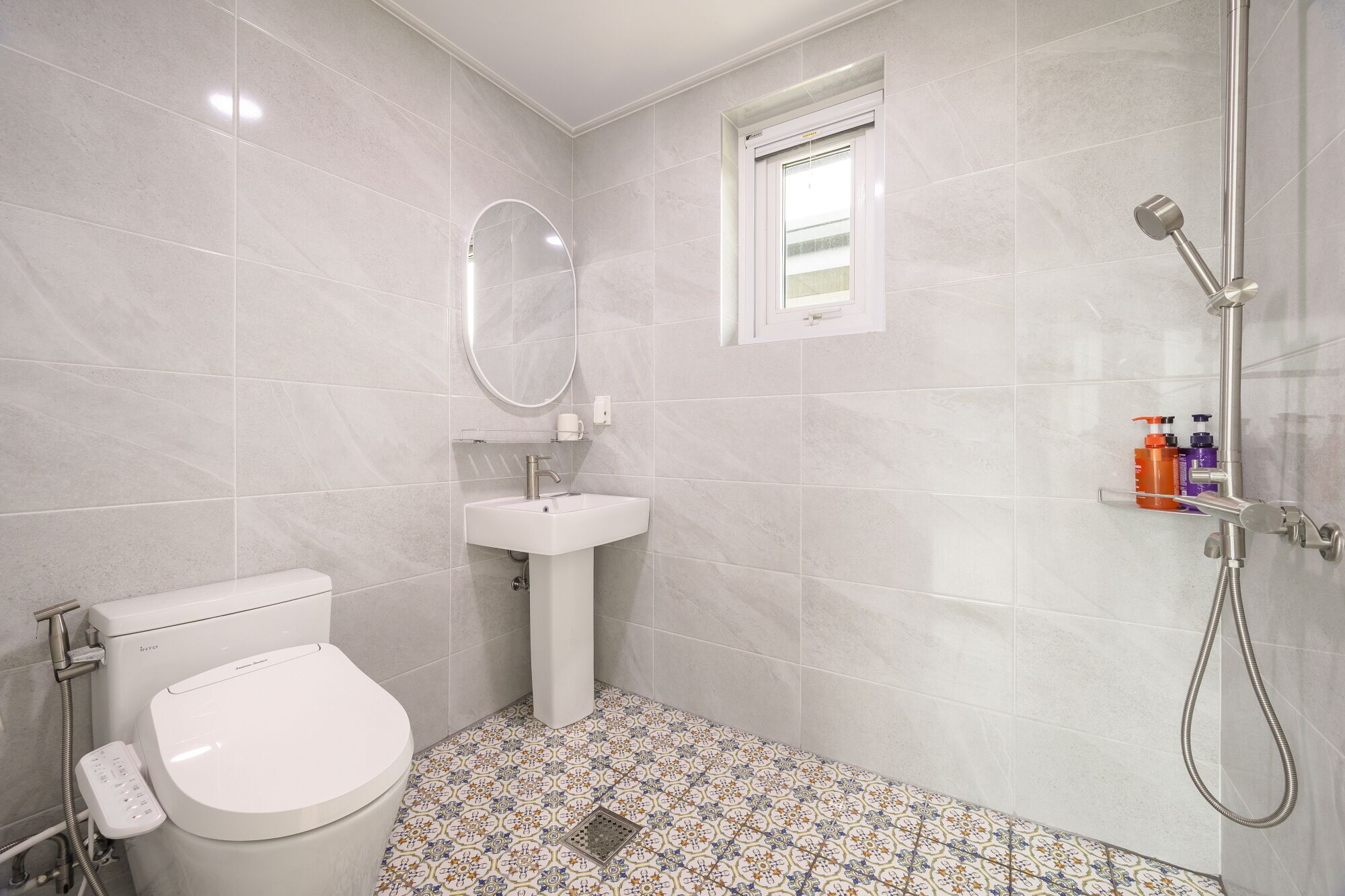 Un baño con inodoro, lavamanos, ducha y baldosas de suelo estampadas.