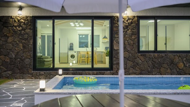 A modern house with a stone exterior, a glass-enclosed kitchen, and a swimming pool with a lounge area. - Gimnyeong stonewall Private Pool Villa (Jeju City)