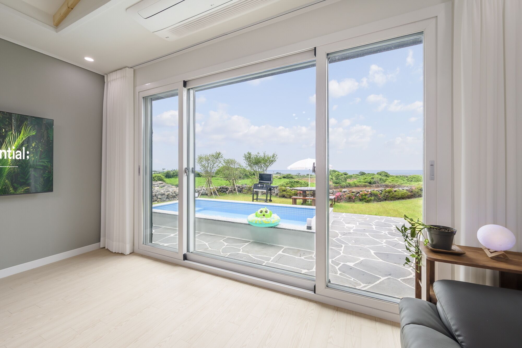 A spacious room with a large sliding glass door leading to a pool area, a comfortable seating area, and a view of the outdoors.