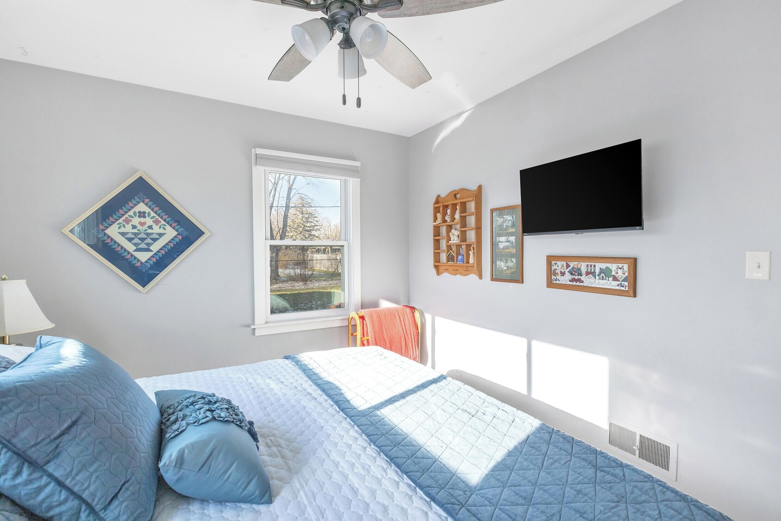 A bedroom with a bed, a ceiling fan, a window, and wall-mounted decorations.