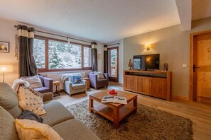 A modern living room with a sofa, armchairs, a coffee table, and a television. - l Ours Bleu Apartments (Vallorcine)